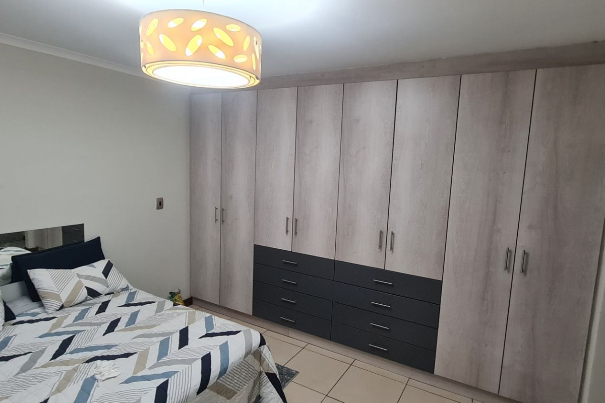 A well-maintained bedroom featuring extensive floor-to-ceiling built-in cabinetry with a modern two-tone wood and charcoal finish and tiled flooring.