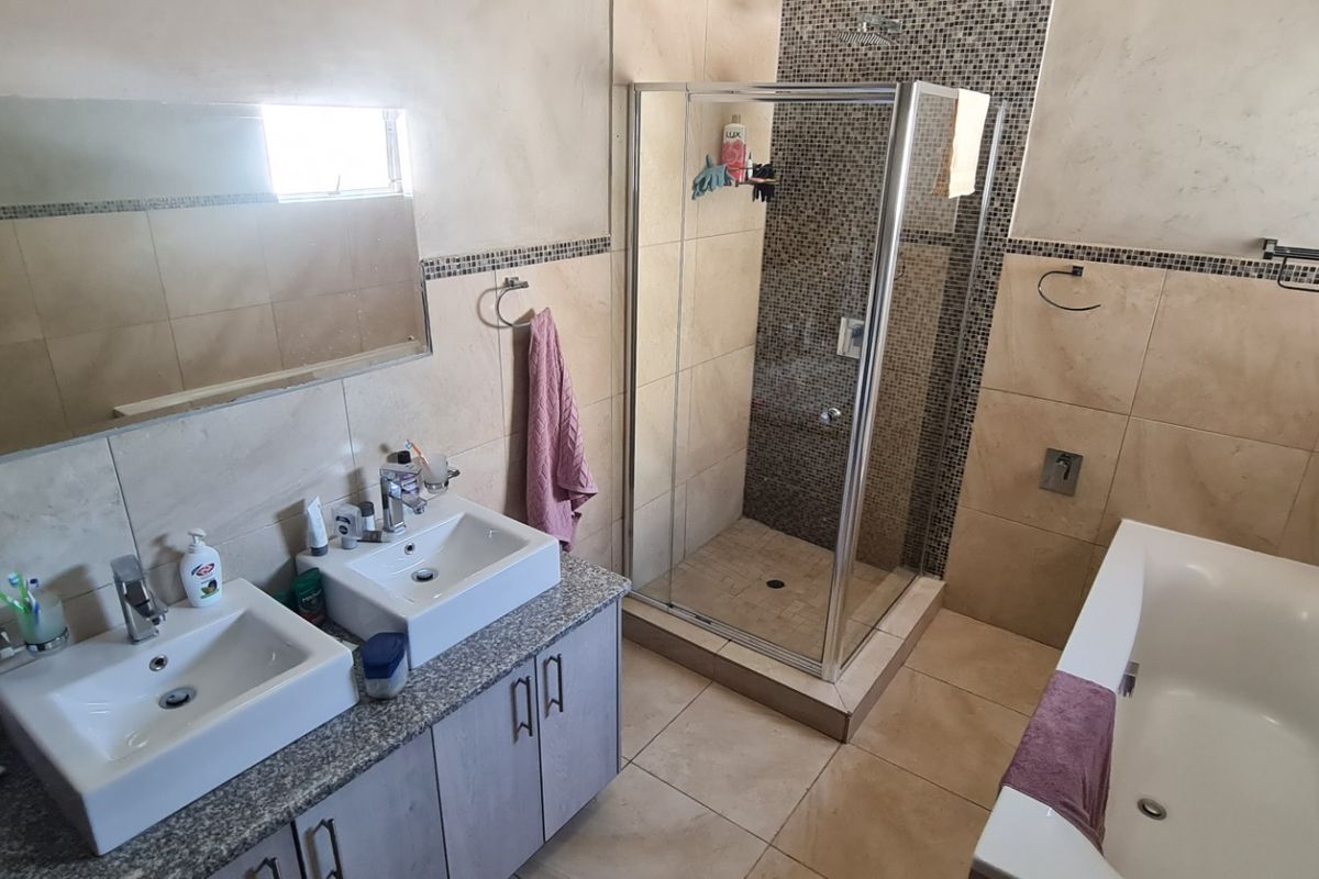 A functional bathroom featuring a double vanity with granite countertop, a glass-enclosed shower, and a separate bathtub with neutral wall and floor tiling.