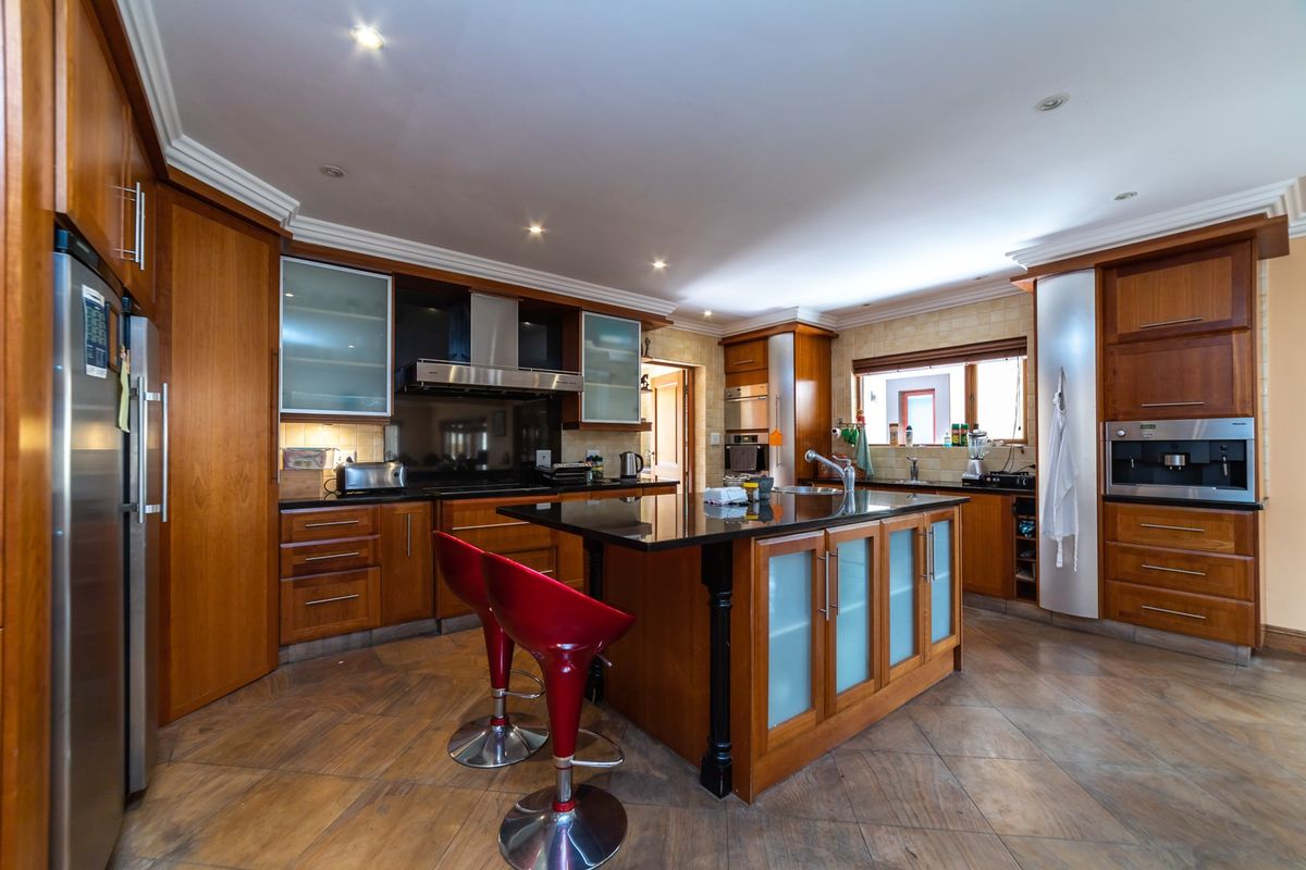 Spacious kitchen featuring warm wood cabinetry, a central island with a dark stone countertop, integrated appliances, and recessed ceiling lighting.