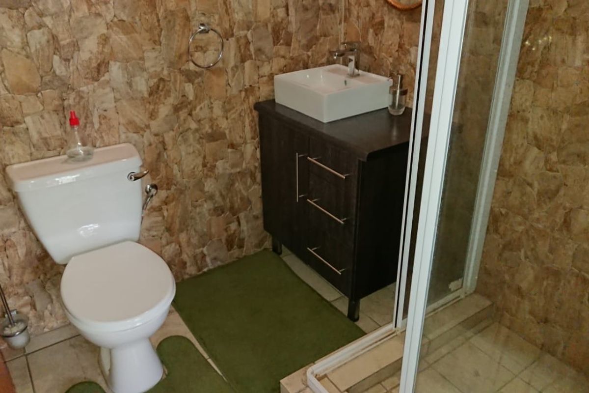 A compact bathroom featuring a vanity with a vessel sink, a standard toilet, and a glass-enclosed shower stall with stone-style wall cladding.