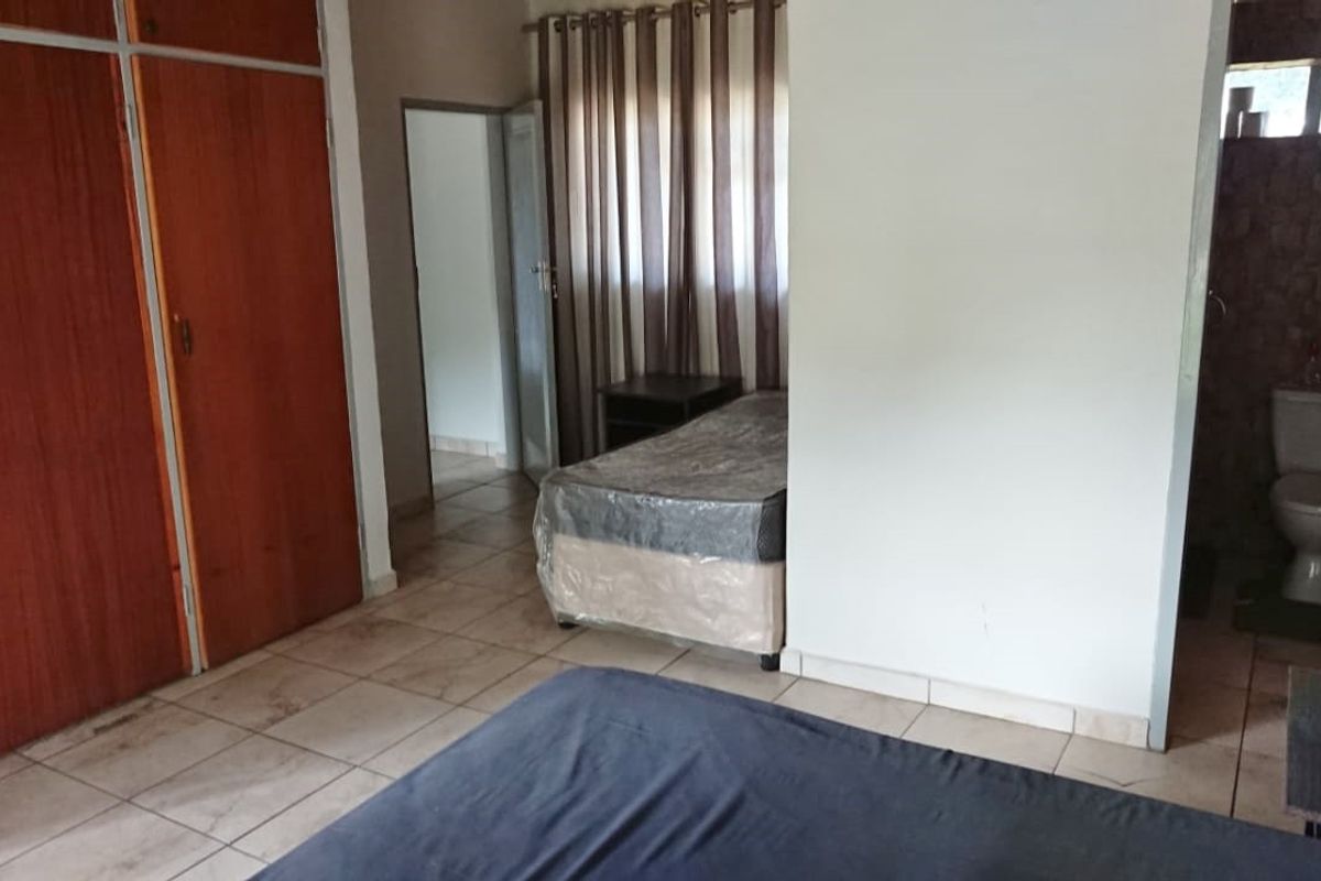 A bedroom featuring built-in wooden cupboards, tiled flooring, and an en-suite bathroom with a toilet.