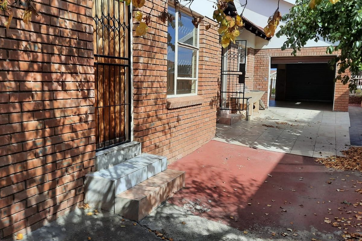 A view of the exterior rear area featuring face-brick walls, tiled entrance steps, a paved patio space, and access to a garage.