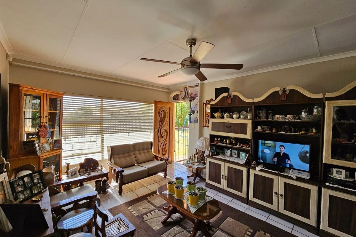 A comfortable living room featuring tiled flooring, a ceiling fan, and large windows that provide natural light.