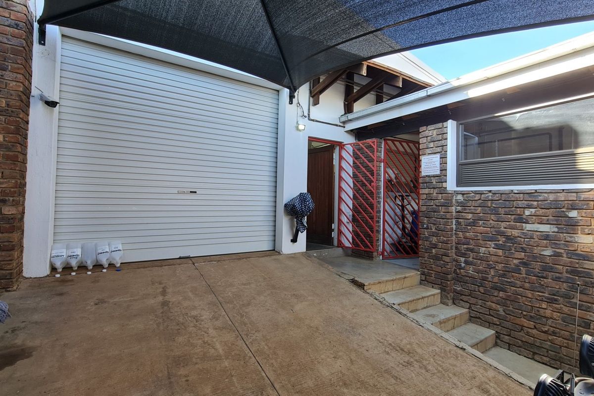 Exterior view of a commercial property featuring a roller shutter door, brick facade, and a covered entrance area with security gates.