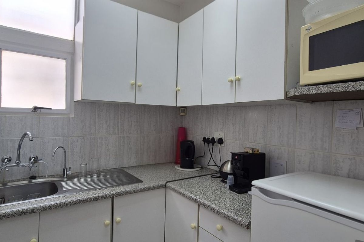 A compact kitchen featuring white cabinetry, granite-look laminate countertops, a stainless steel sink with mixer tap, and tiled splashbacks.