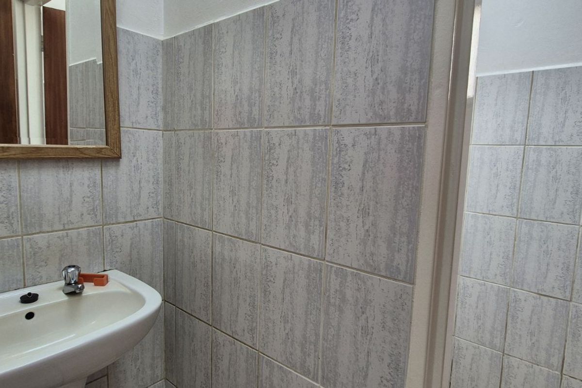 A functional bathroom featuring tiled walls, a pedestal basin with chrome taps, and a wall-mounted mirror.