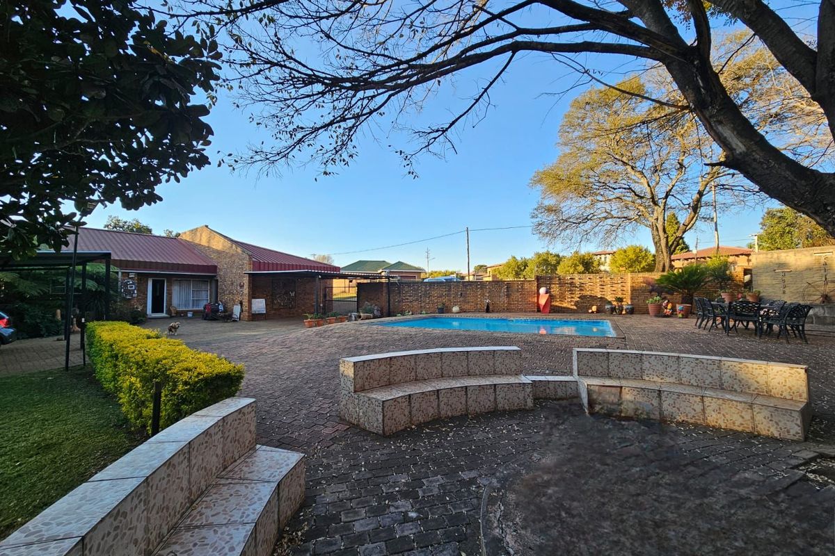 Spacious rear garden area featuring a swimming pool, paved courtyard, and built-in tiled seating, ideal for outdoor entertaining.