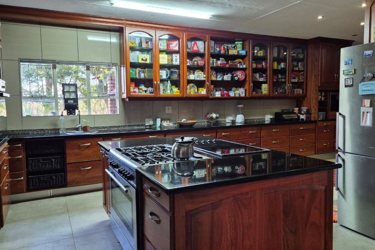 Spacious kitchen featuring dark wood cabinetry, granite countertops, a central island with a built-in gas hob and oven, and ample storage space.