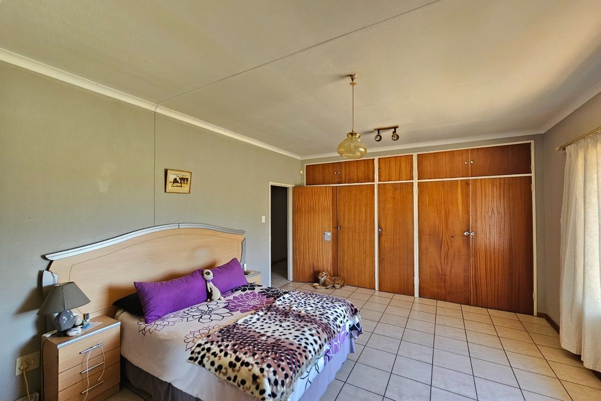 Spacious bedroom featuring built-in wooden cupboards, tiled flooring, and a central pendant light fixture.