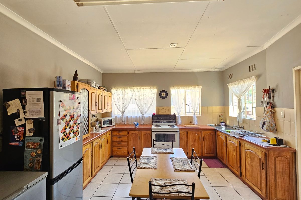 A spacious kitchen featuring traditional wooden cabinetry, tiled flooring, and a central dining area, offering a functional layout with ample storage space.