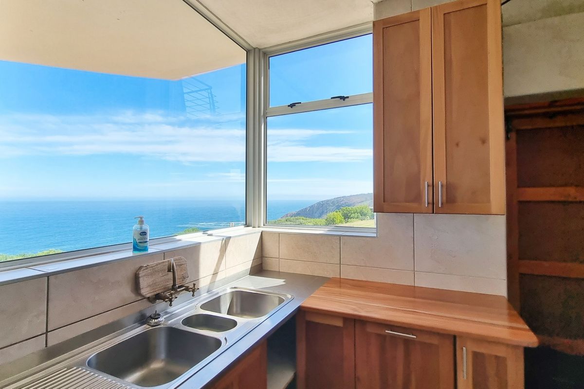 Kitchen area featuring wooden cabinetry, stainless steel double sink, and expansive windows offering panoramic ocean and coastal views.