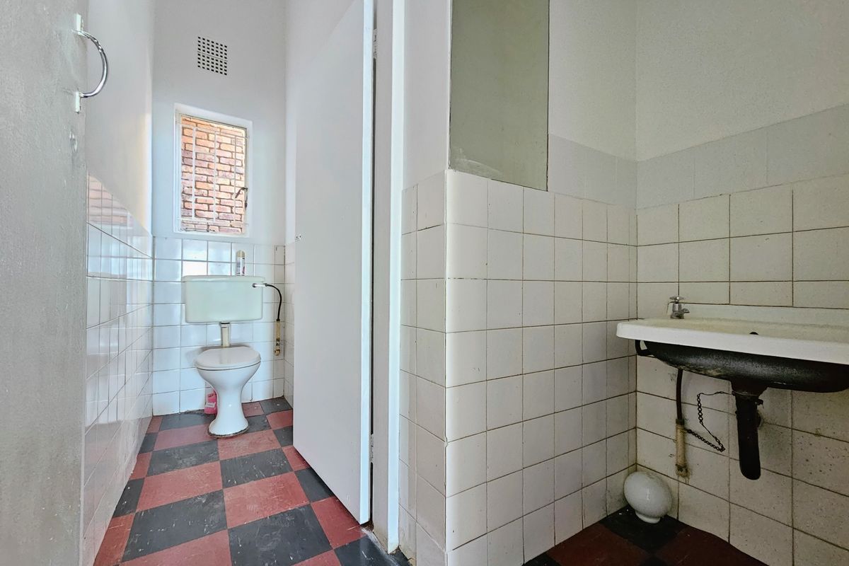 A functional bathroom featuring a wall-mounted basin, toilet, and tiled finishes, requiring cosmetic updates to modernize the space.