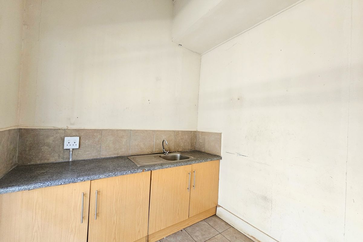 A compact kitchenette area featuring light wood cabinetry, a granite-look countertop, a stainless steel sink, and tiled flooring.