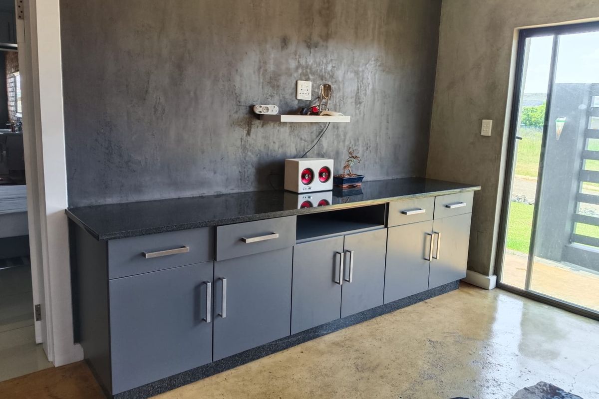 A modern living area featuring a built-in grey cabinetry unit with a dark stone countertop, polished concrete flooring, and a sliding glass door.