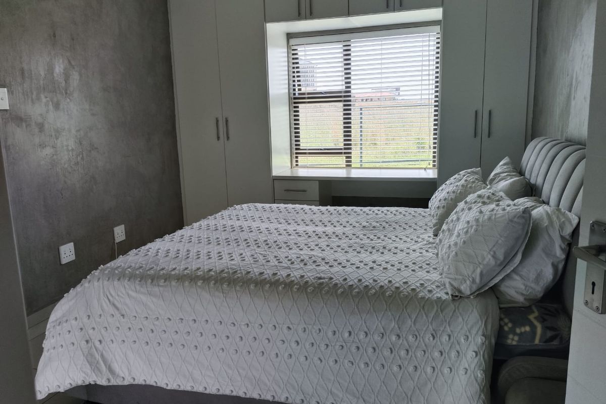 A well-maintained bedroom featuring built-in floor-to-ceiling wardrobes, a window seat with integrated storage, and a textured feature wall.