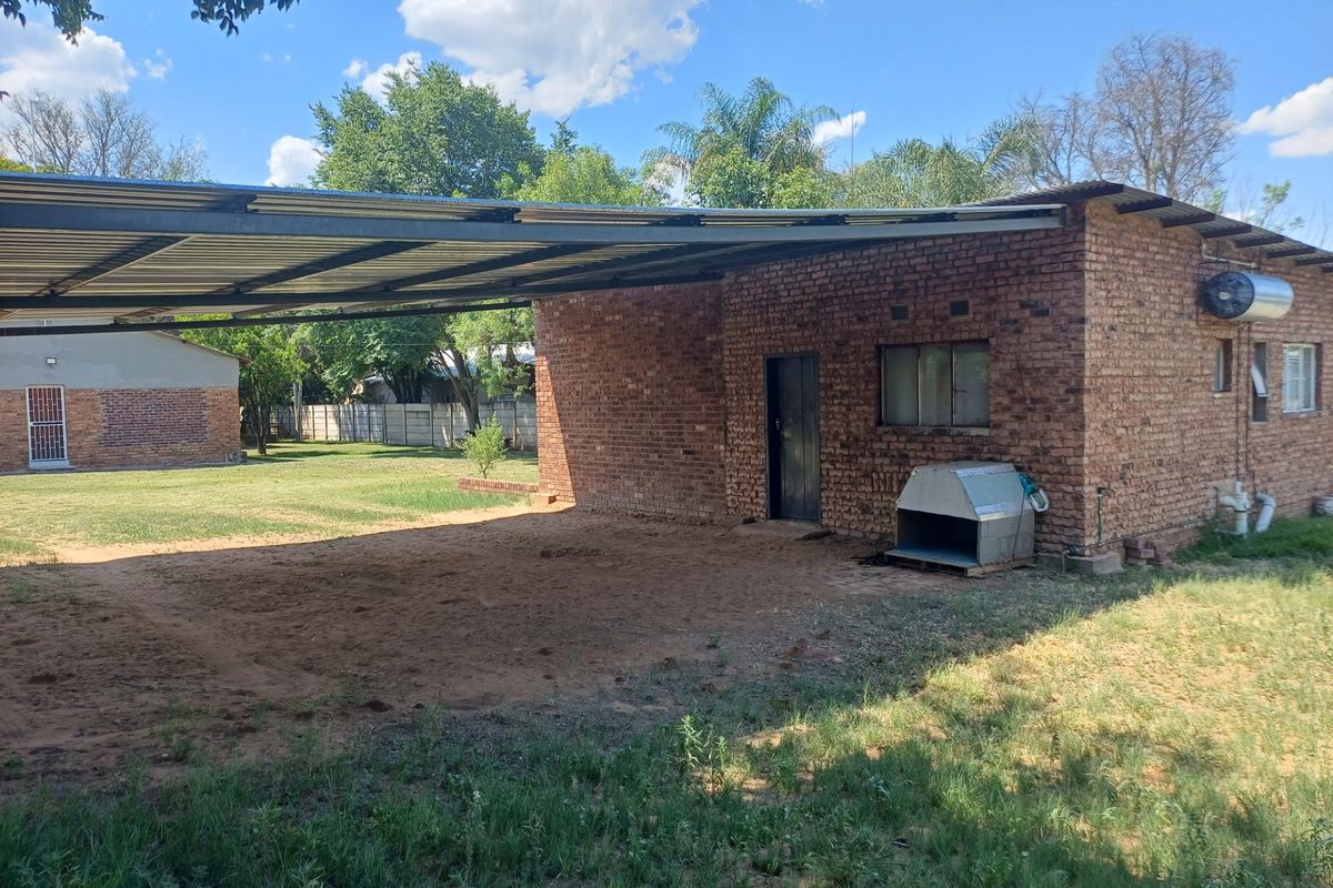 Exterior view of a brick-built structure featuring a large attached carport, providing covered parking space within a spacious garden setting.