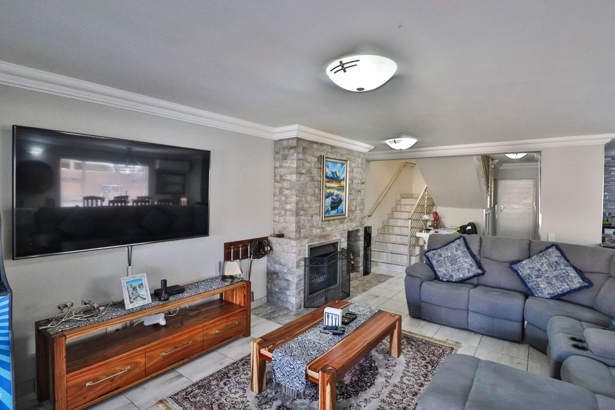 Spacious living room featuring a stone-clad fireplace, tiled flooring, and crown molding, providing a comfortable and inviting atmosphere.