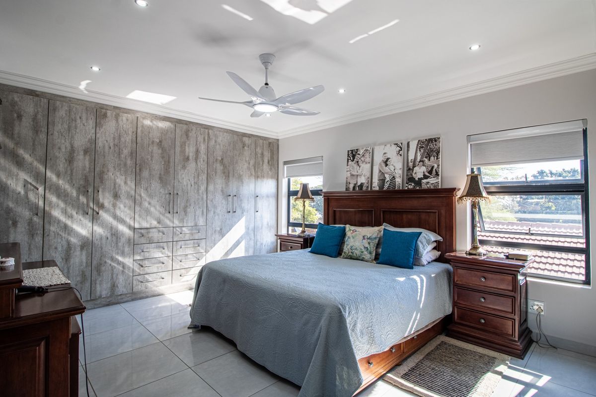 Spacious bedroom featuring extensive built-in cabinetry with a modern wood-grain finish, tiled flooring, recessed ceiling lighting, and a central ceiling fan.
