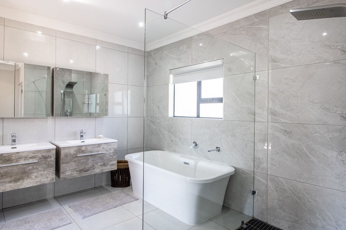 Modern bathroom featuring a freestanding bathtub, glass-enclosed shower, and dual floating vanity units with integrated mirrors and contemporary grey tiling.