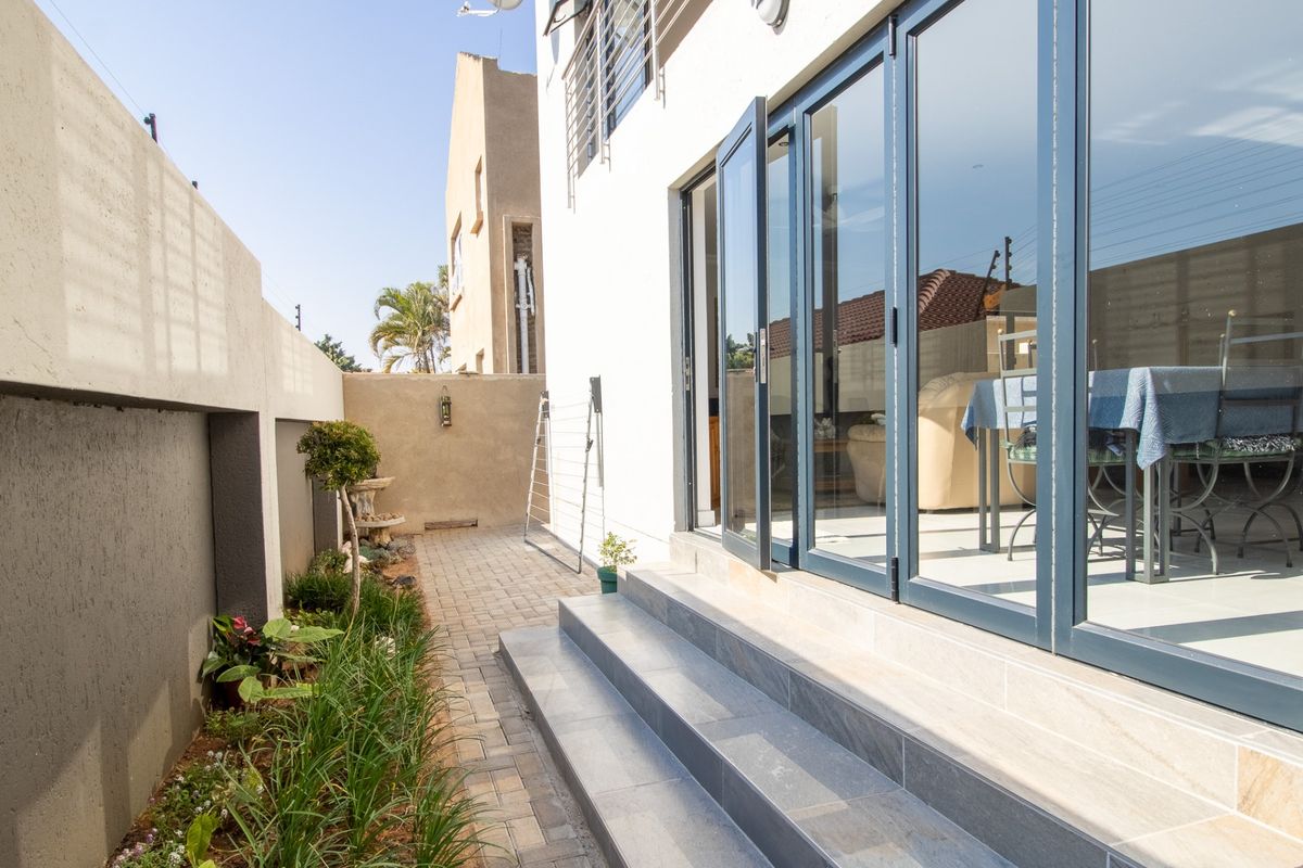 A side exterior view featuring paved pathways, landscaped garden beds, and modern aluminium stacker doors leading into the home.