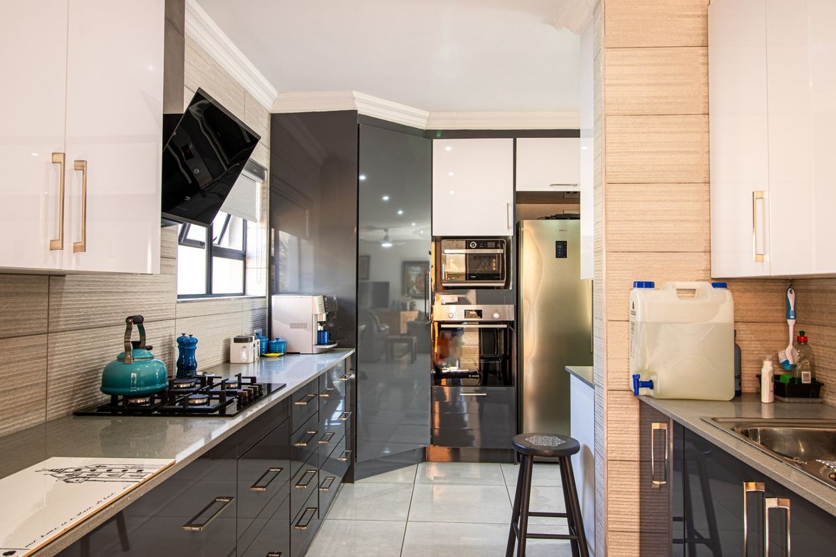 Modern kitchen featuring high-gloss cabinetry, stone countertops, built-in oven, microwave, and gas hob with a sleek extractor fan.