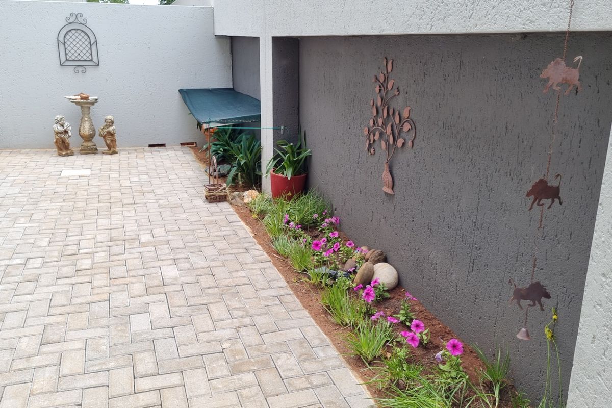 A paved courtyard area featuring a textured boundary wall with integrated garden bed and decorative metal wall art.