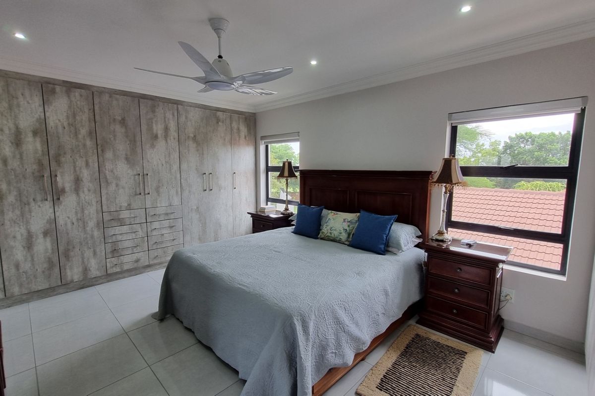 A well-maintained bedroom featuring extensive built-in cabinetry with a modern wood-grain finish, tiled flooring, and large windows providing natural light.