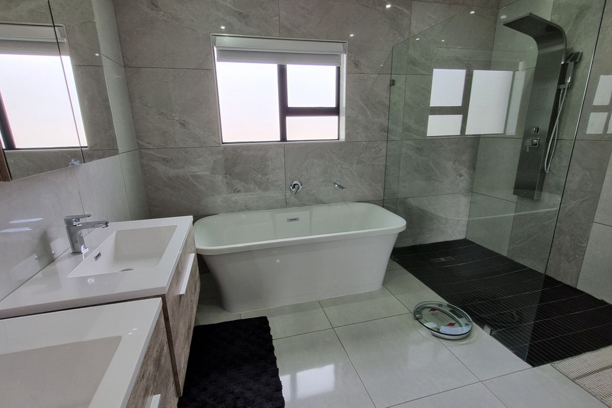 Modern bathroom featuring a freestanding bathtub, a glass-enclosed walk-in shower with a rainfall showerhead, and a double vanity with stone countertops.
