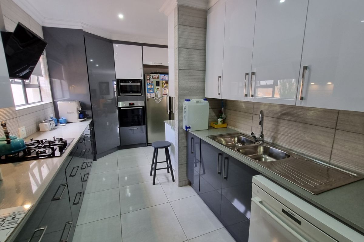 Modern galley-style kitchen featuring high-gloss cabinetry, stone countertops, integrated oven, built-in microwave, gas hob, and a double stainless steel sink.
