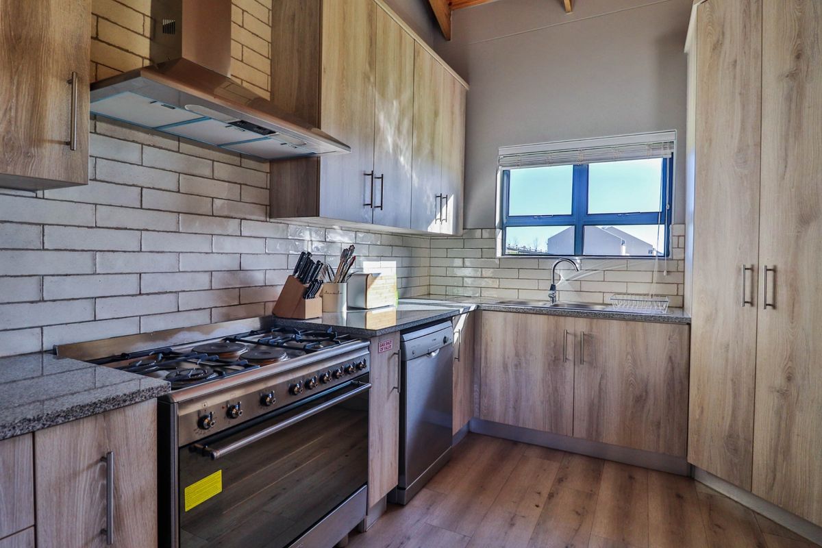 Modern kitchen featuring light wood-grain cabinetry, granite countertops, subway tile backsplash, and a stainless steel gas stove with extractor fan.