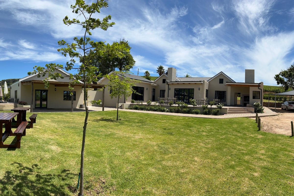 A wide-angle view of the rear farm property featuring a spacious lawn, paved patio area, and multiple building structures with modern finishes.