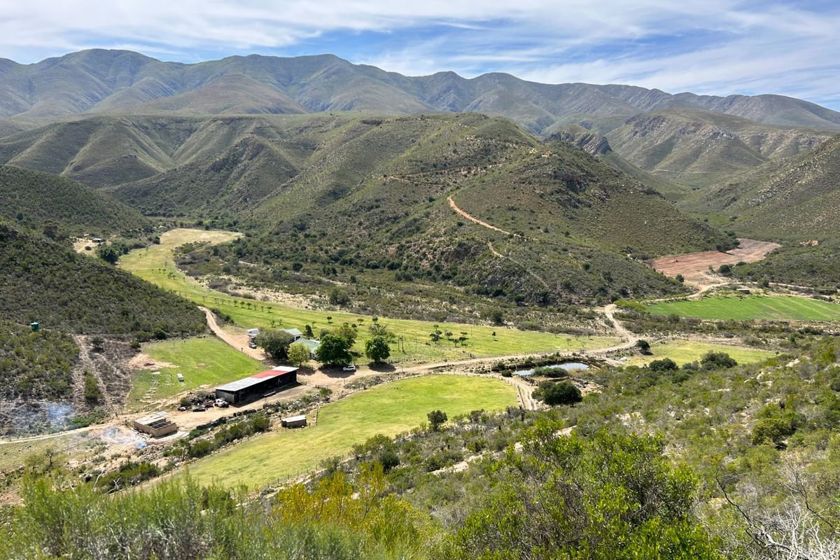 Expansive aerial view of the farm property, showcasing the surrounding mountain landscape, open grazing fields, and existing farm infrastructure.