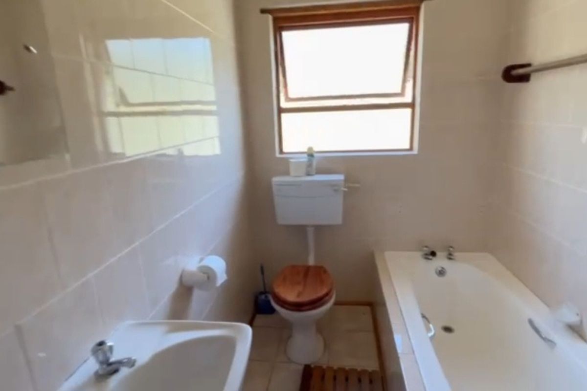 A functional bathroom featuring a built-in bathtub, a standard toilet, and a wall-mounted basin with tiled walls.