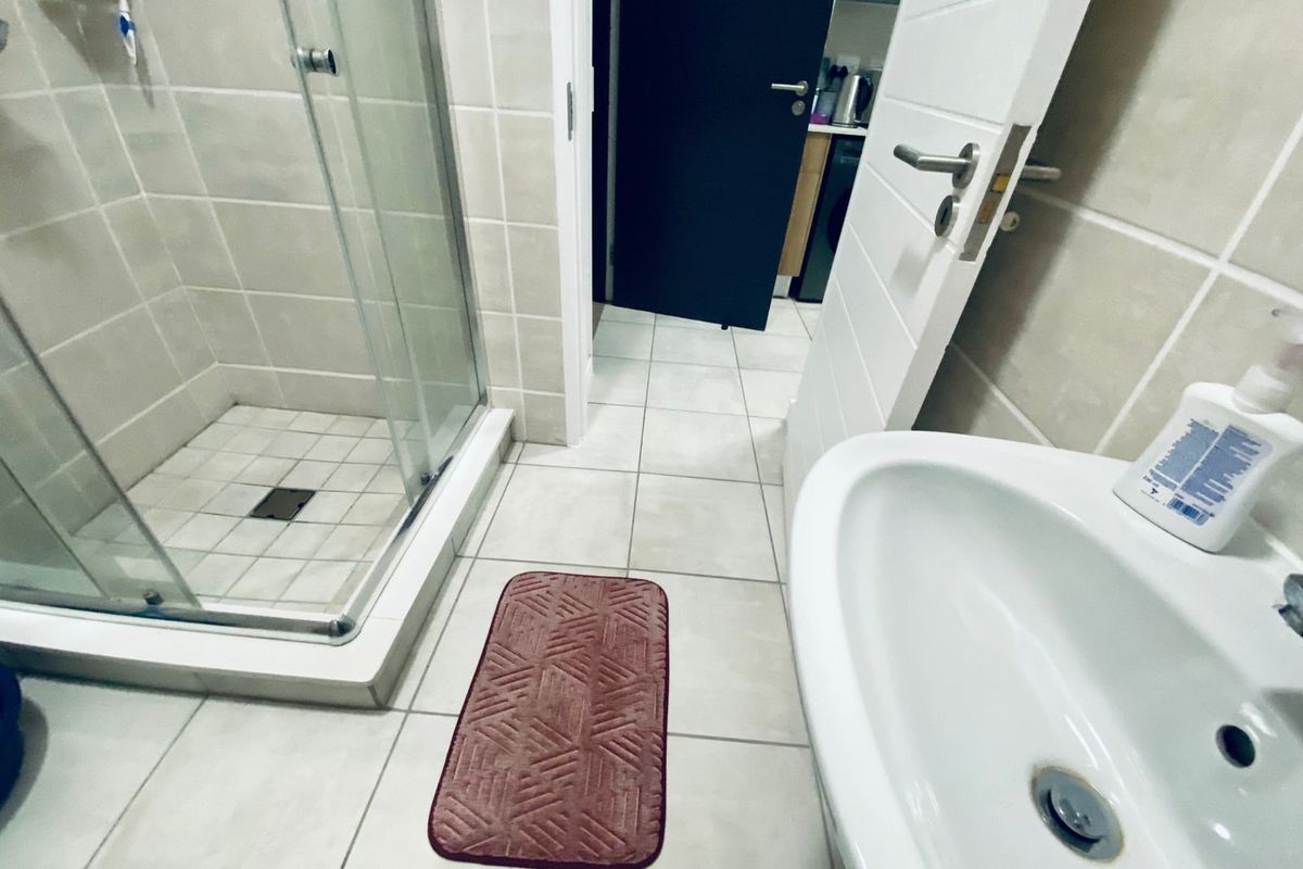 A functional bathroom featuring a glass-enclosed shower stall, ceramic floor tiling, and a pedestal washbasin with modern hardware.