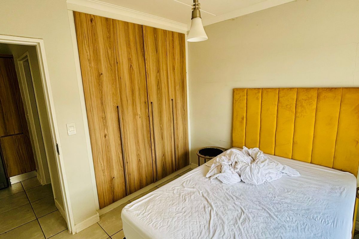 A bedroom featuring built-in wooden cupboards, tiled flooring, and a pendant light fixture.