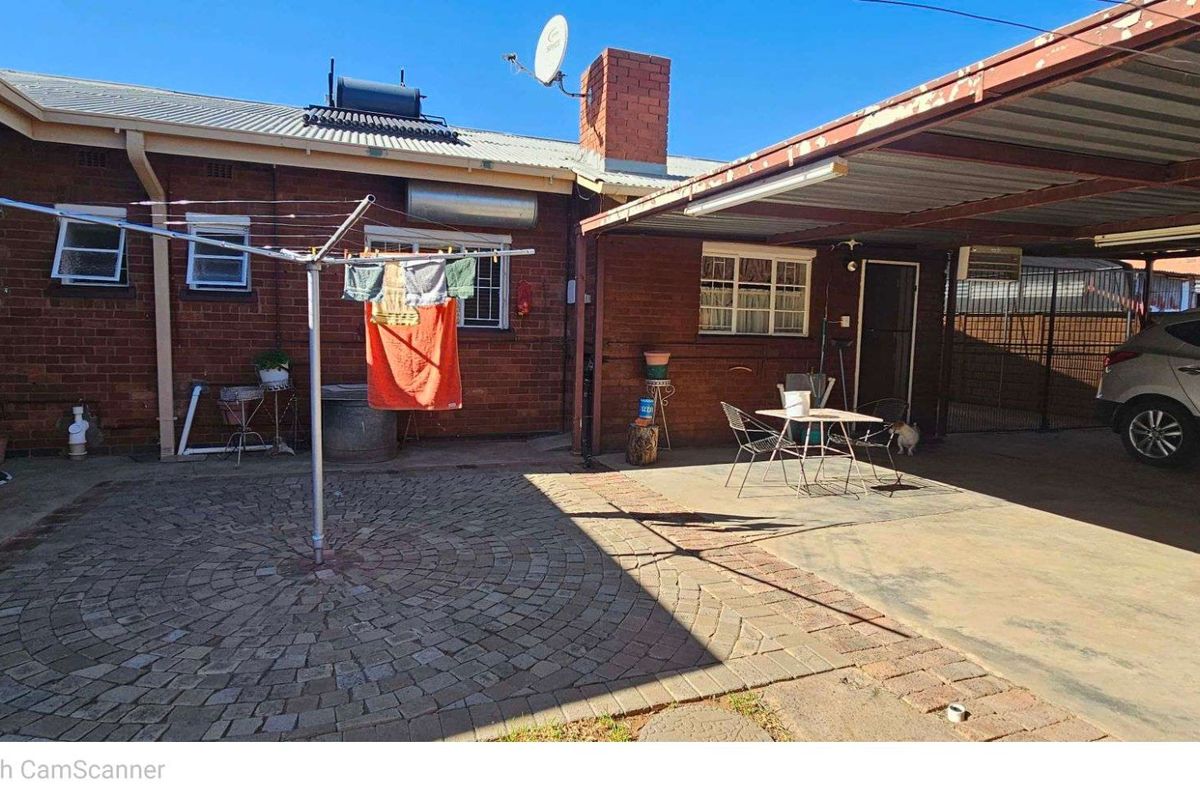 Rear exterior area featuring a paved courtyard, brick facade, and a covered carport structure.