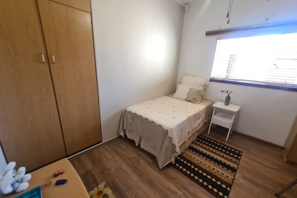 A functional bedroom featuring built-in wooden cabinetry, laminate flooring, and a window with fitted blinds.