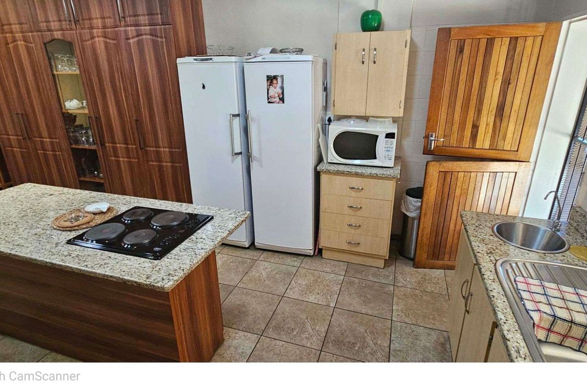 Kitchen featuring granite countertops, a central island with a built-in electric hob, tiled flooring, and wooden cabinetry.