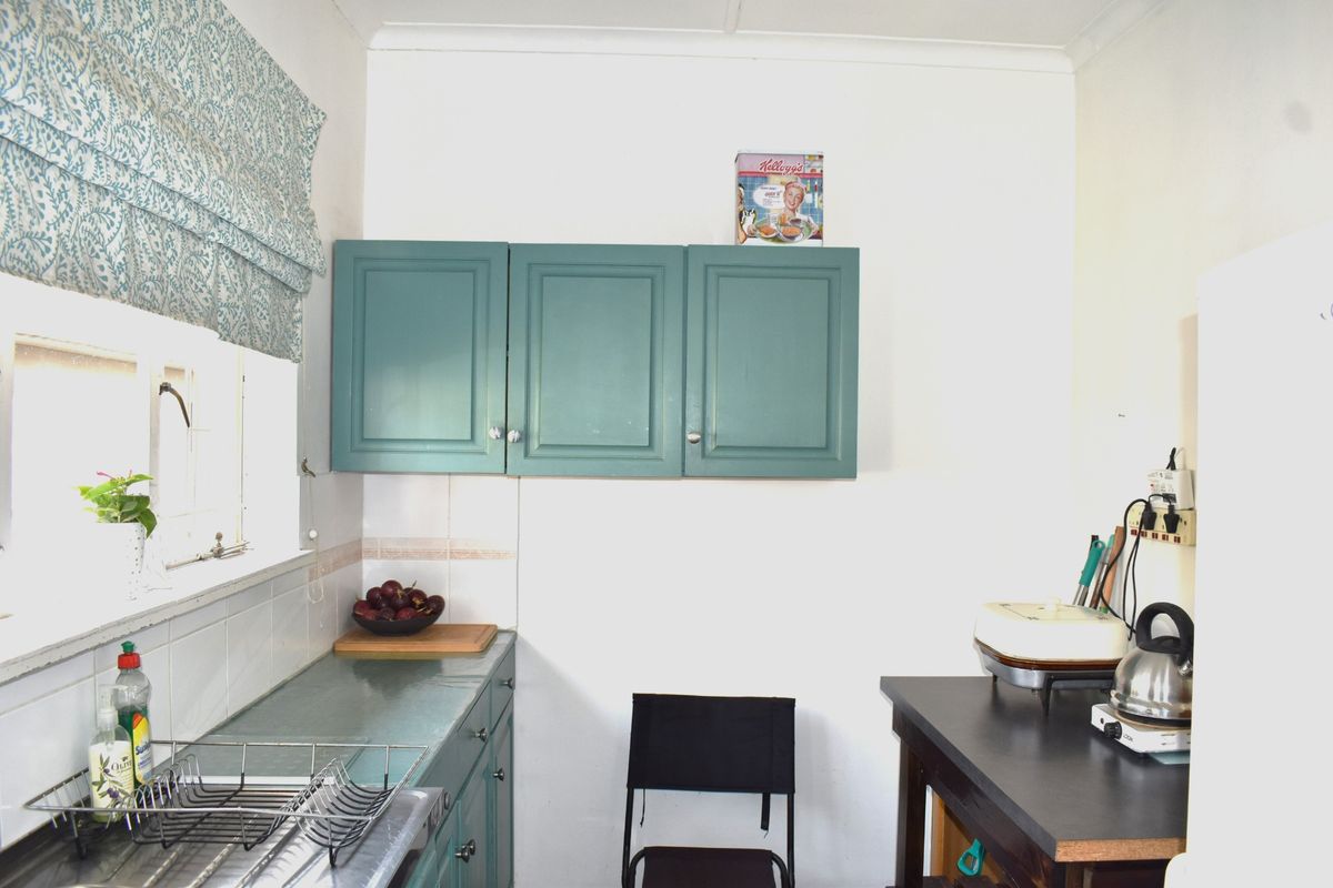 A functional kitchen area featuring teal-painted cabinetry, tiled splashbacks, and a compact layout with integrated counter space.