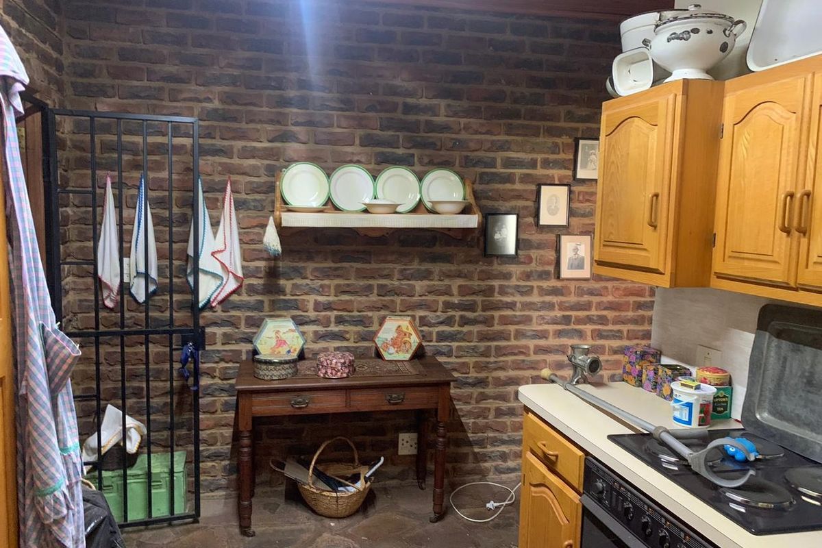 Rustic kitchen area featuring exposed brick walls, wooden cabinetry, a built-in oven with hob, and stone flooring.