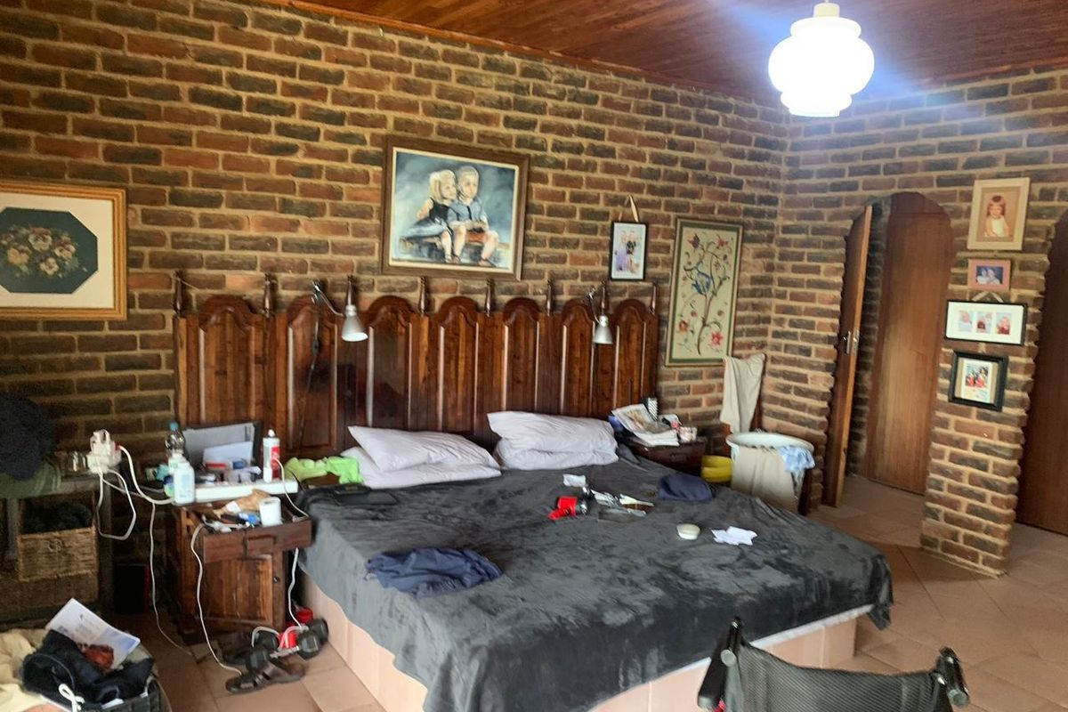 A rustic bedroom featuring exposed face-brick walls, a timber-paneled ceiling, and tiled flooring, providing a traditional farm-style aesthetic.