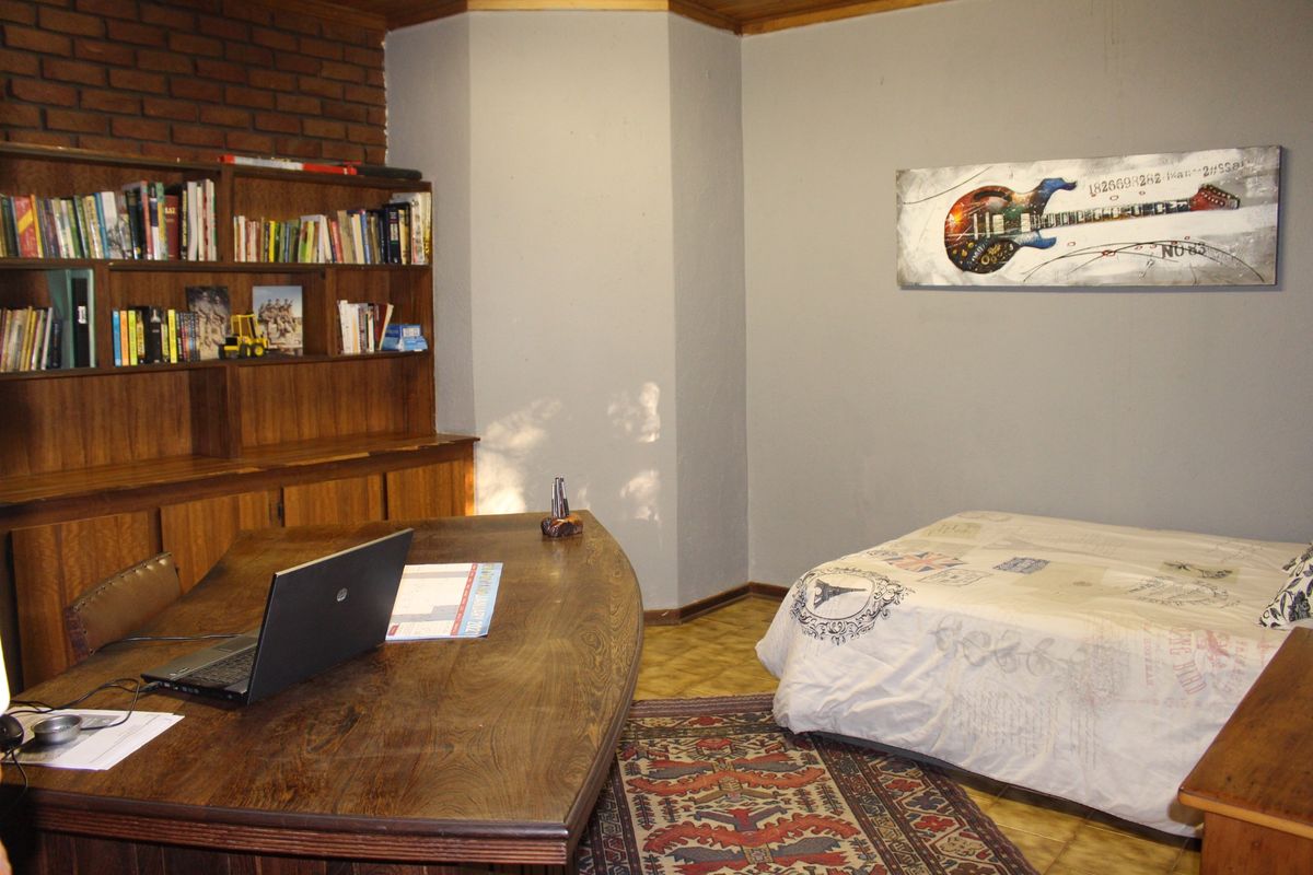 A multi-purpose bedroom featuring built-in wooden shelving and parquet flooring, currently utilized as a combined sleeping and workspace area.
