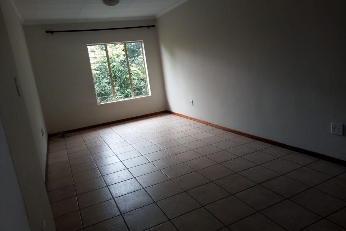 A spacious, empty living area featuring neutral ceramic floor tiles, a large window with security bars, and a simple ceiling-mounted light fixture.