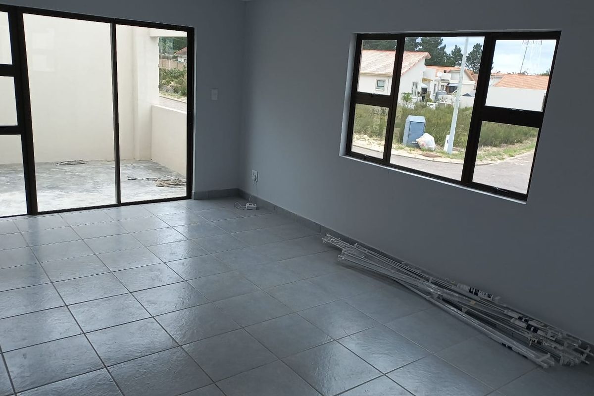 A bright, empty living area featuring neutral floor tiles, large aluminium-framed windows, and sliding glass doors leading to an outdoor patio space.