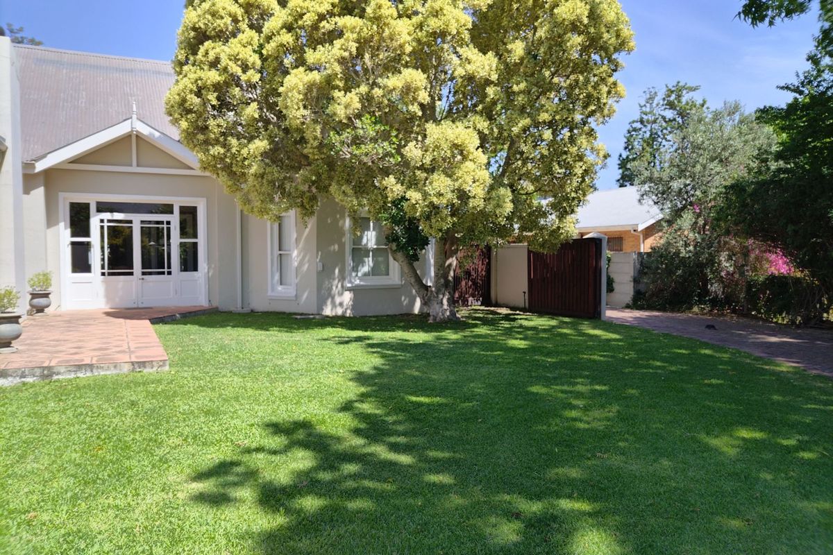 A well-maintained rear garden featuring a lush lawn, mature tree, paved patio area, and direct access to the home through double glass doors.