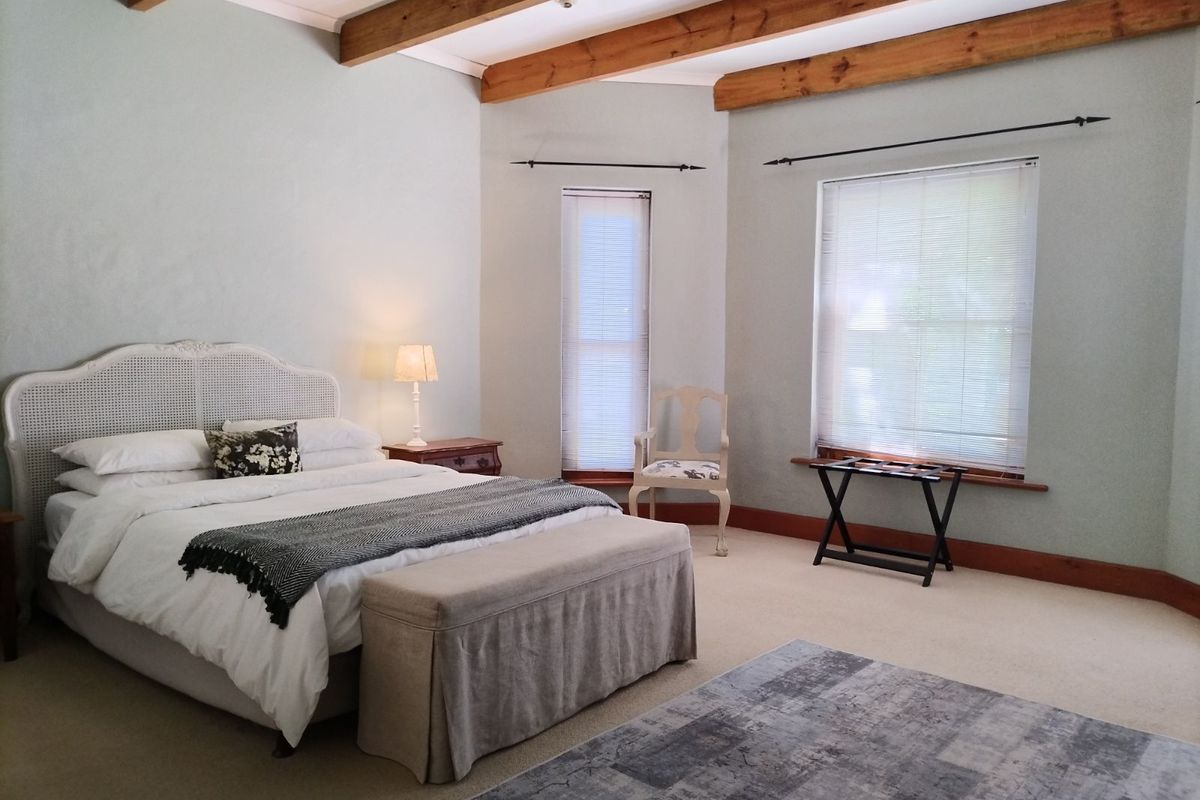 Spacious bedroom featuring exposed timber ceiling beams, neutral carpeting, and large windows with fitted blinds, offering a bright and comfortable living space.
