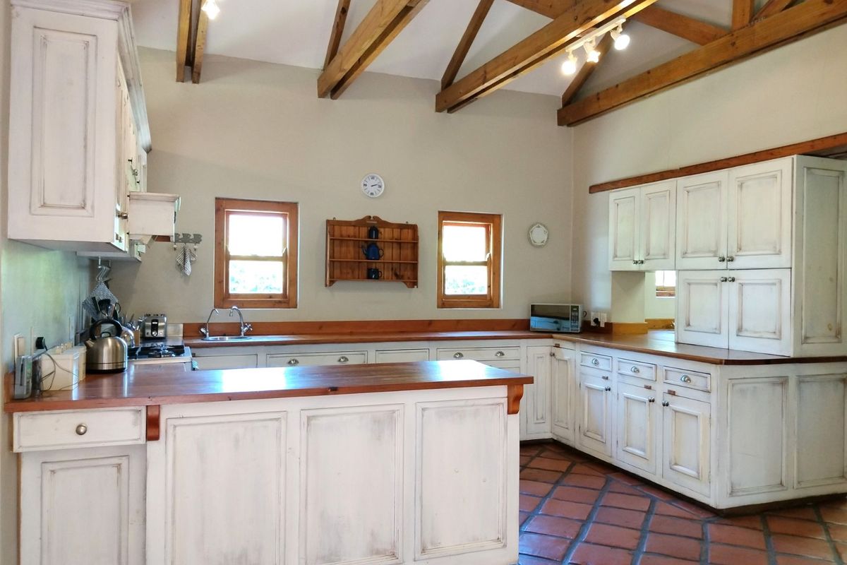 Spacious country-style kitchen featuring distressed white cabinetry, warm timber countertops, terracotta floor tiles, and exposed timber roof trusses.
