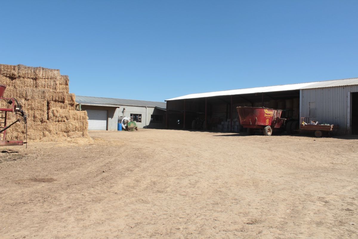 A functional farm yard featuring large storage sheds, corrugated metal structures, and open-air storage areas for agricultural equipment and hay bales.