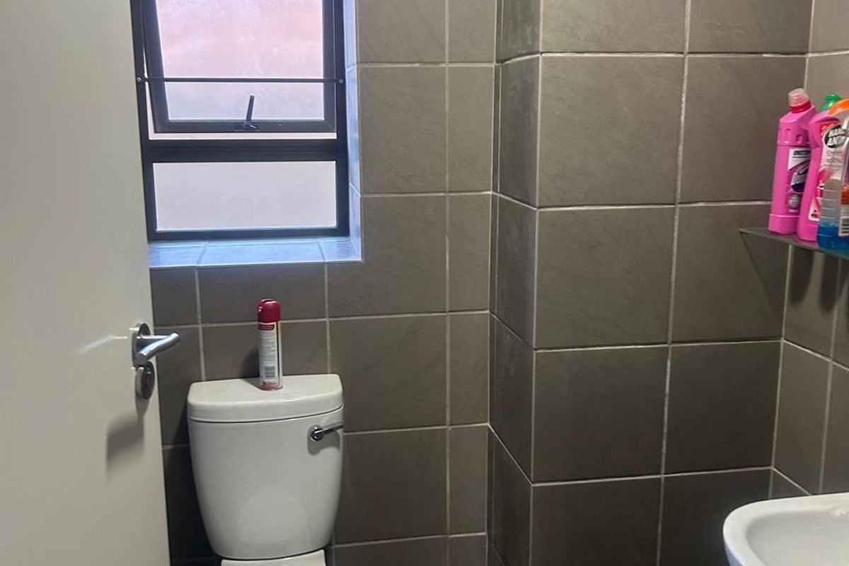A compact office restroom featuring dark grey wall and floor tiling, a white pedestal basin, and a standard toilet.
