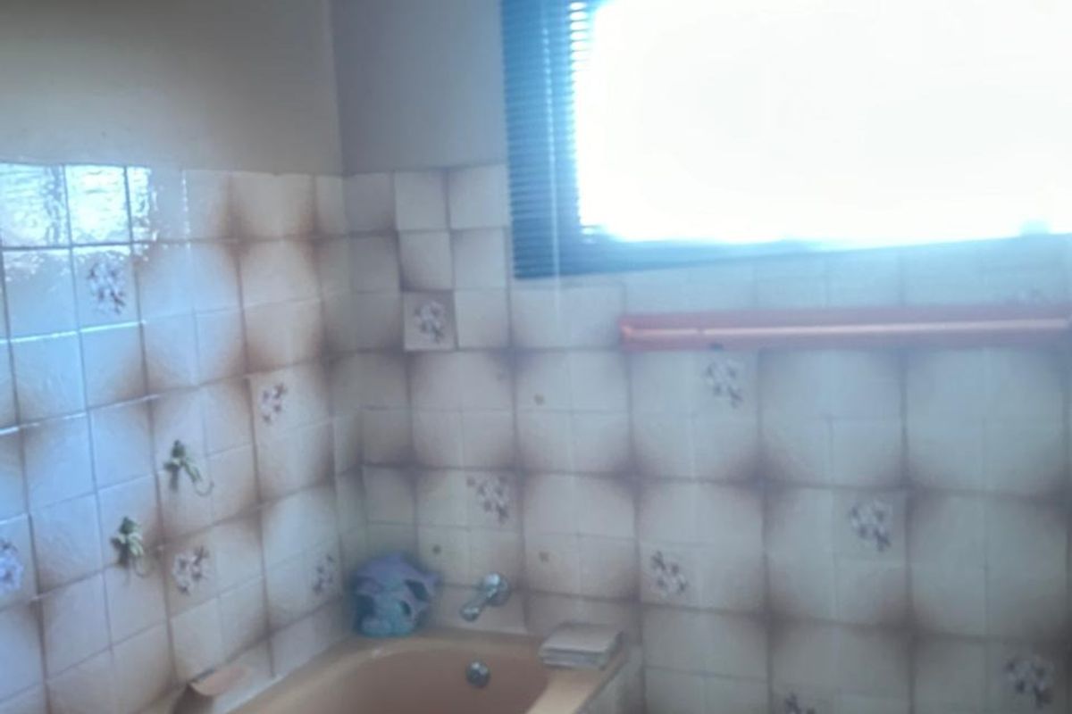A dated bathroom featuring a built-in bathtub with integrated chrome fixtures and patterned wall tiles, requiring modernization.